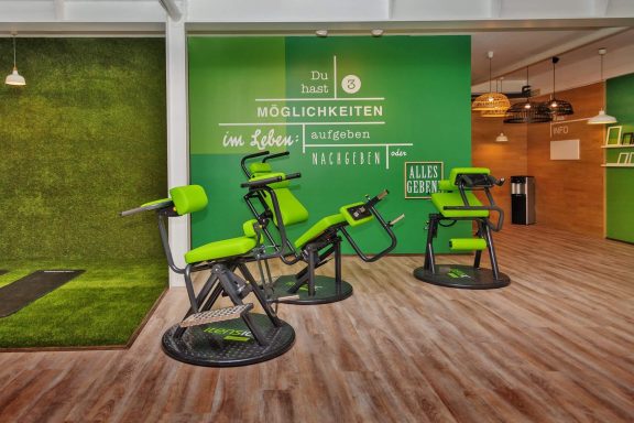 Drei grüne Fitnessgeräte in einem modernen, hellen Raum mit grüner Wand.