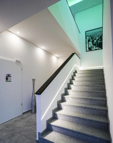 Helle Treppe mit grauem Teppich und grünem Licht, an einer Wand ein schwarzes Bild.